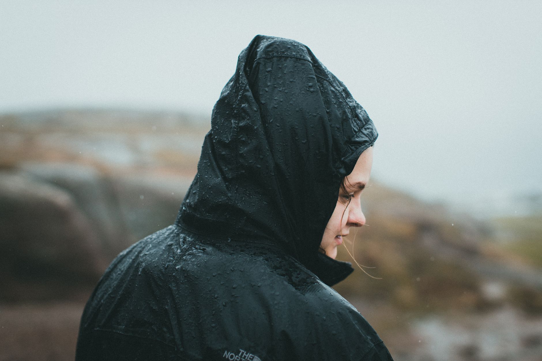 Randonneuse de profil en veste de pluie à capuche sous une averse soutenue
