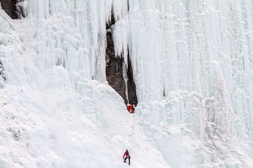 Grimpeur engagé dans une cascade de glace des Rocheuses canadiennes, où le tissu frotte en continu contre le rocher et la glace.