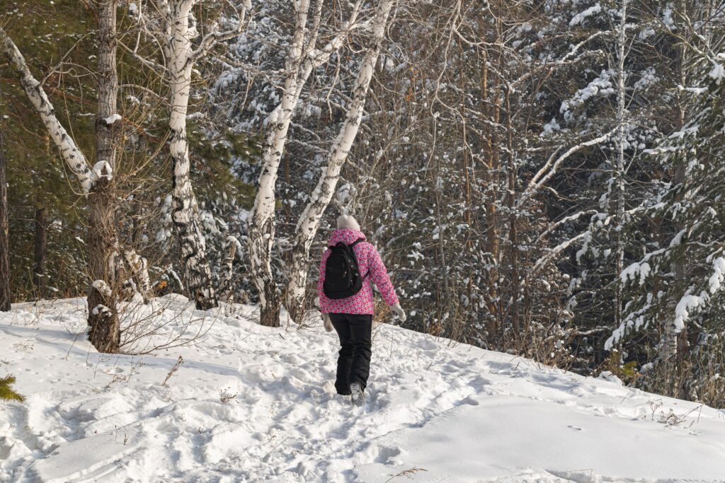 Randonneuse en doudoune progressant sur un sentier forestier enneigé en hiver.