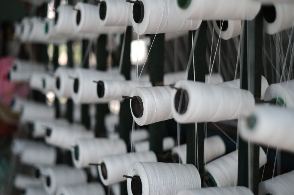 Bobines de fil blanc alignées sur un métier, dans un atelier textile.