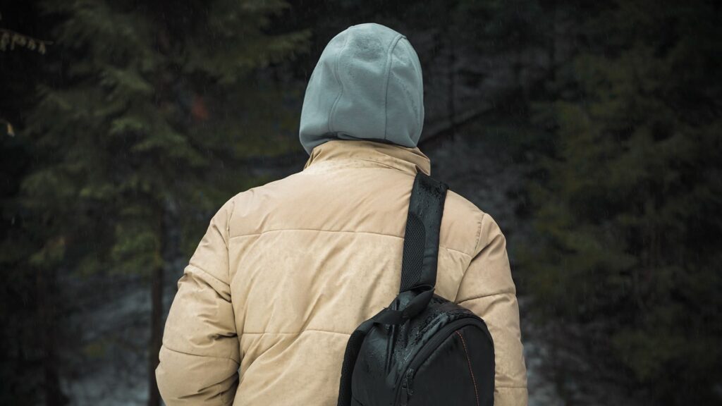 Marcheur avec un sac à dos et une veste à capuche progressant sous la pluie sur un sentier forestier.