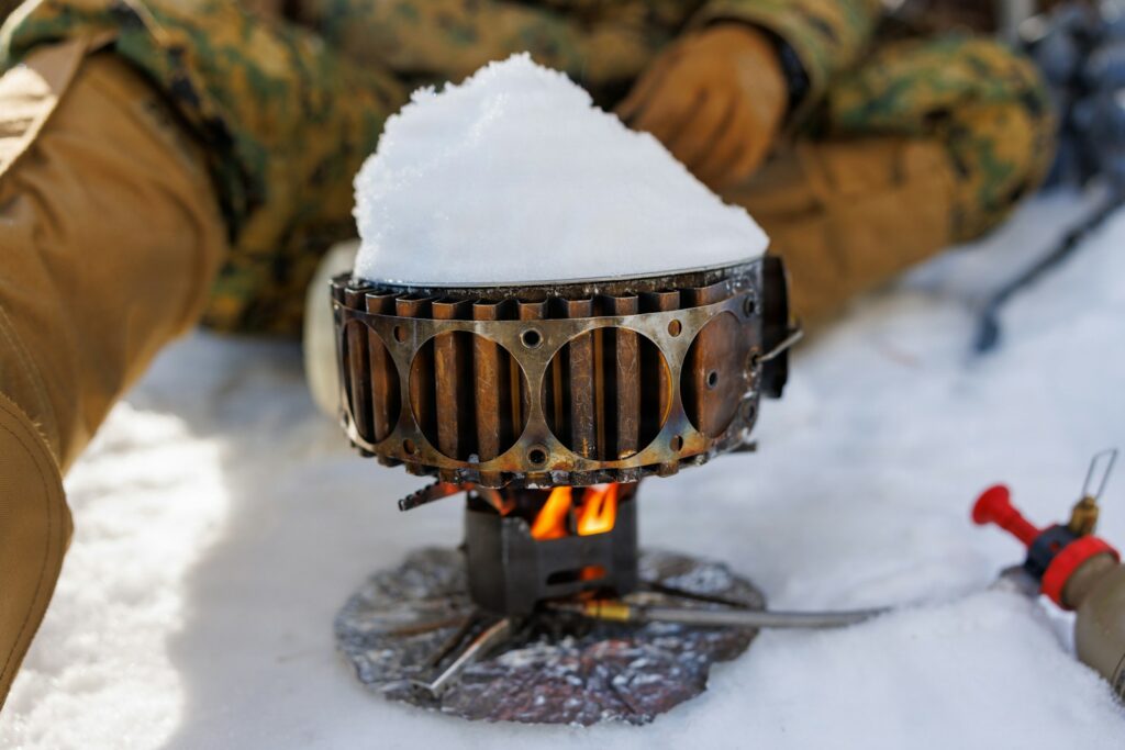Réchaud allumé posé dans la neige, une casserole remplie de neige sur la flamme